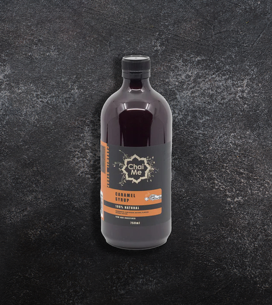 A bottle of Chai Me caramel coffee syrup on a textured dark background.